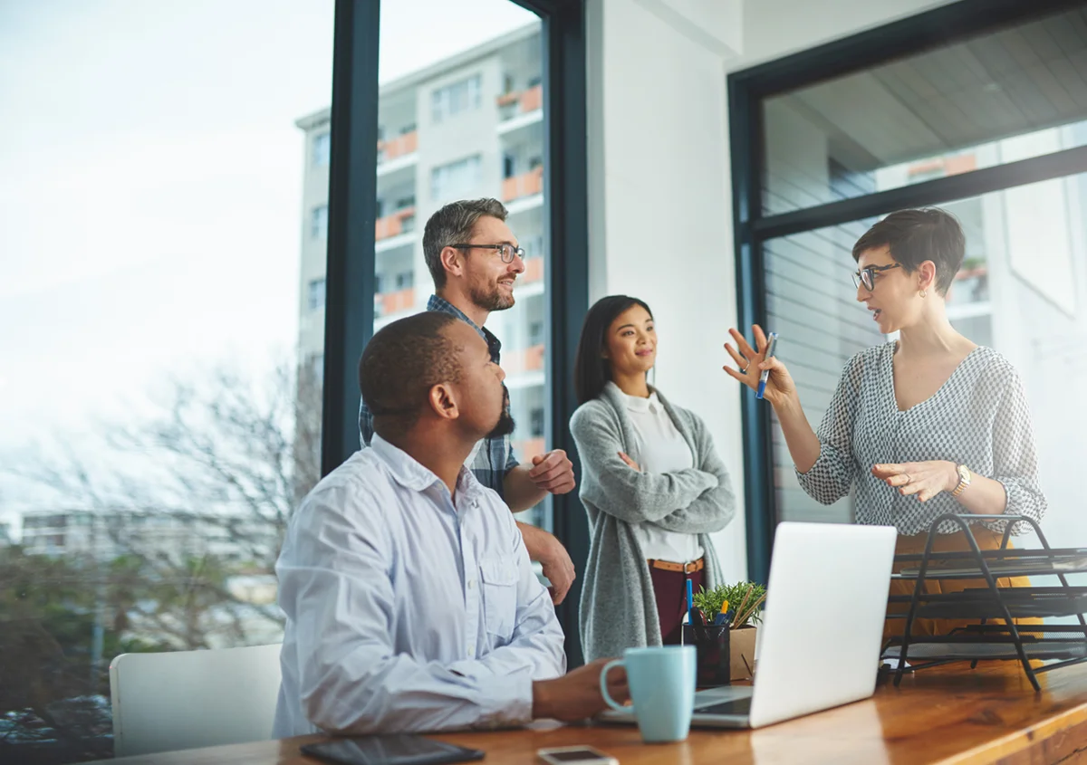 Business team meeting around a table with a laptop while one person leads the discussion.