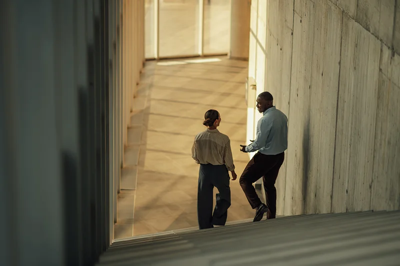 Two professionals talking inside a modern building with warm natural light.