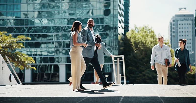 Professionals walking through an urban plaza with modern glass buildings in the background.