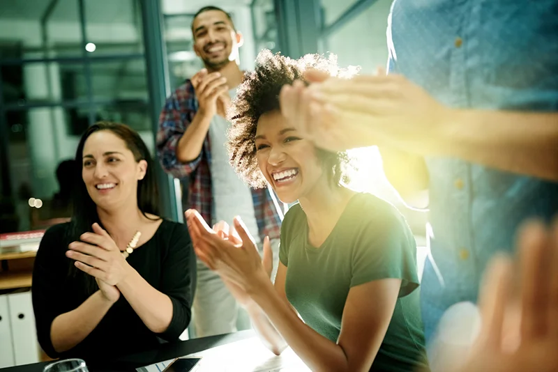 Professionals smiling and clapping during an office meeting.