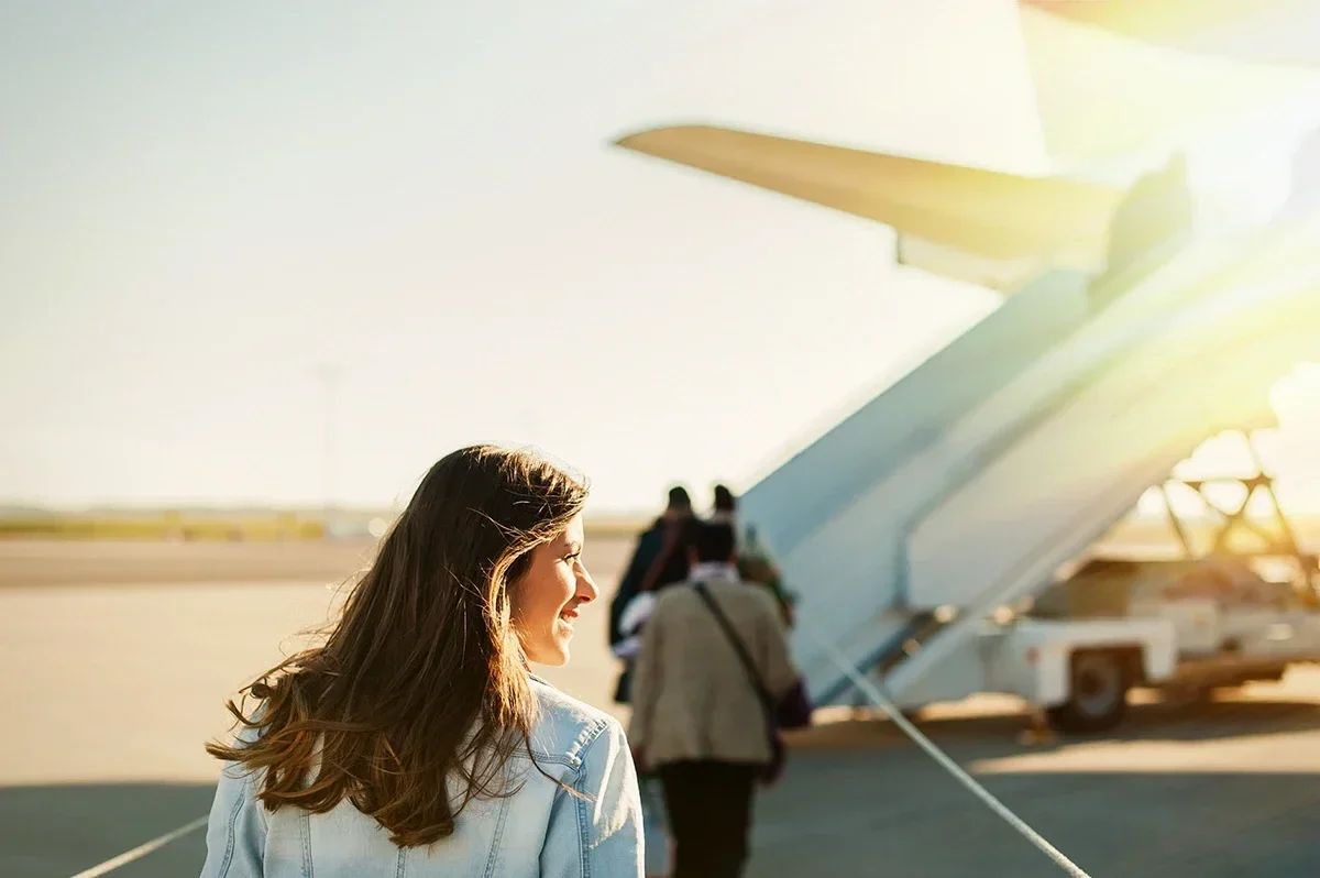 Woman walking toward an airplane on an airport runway in warm sunlight.